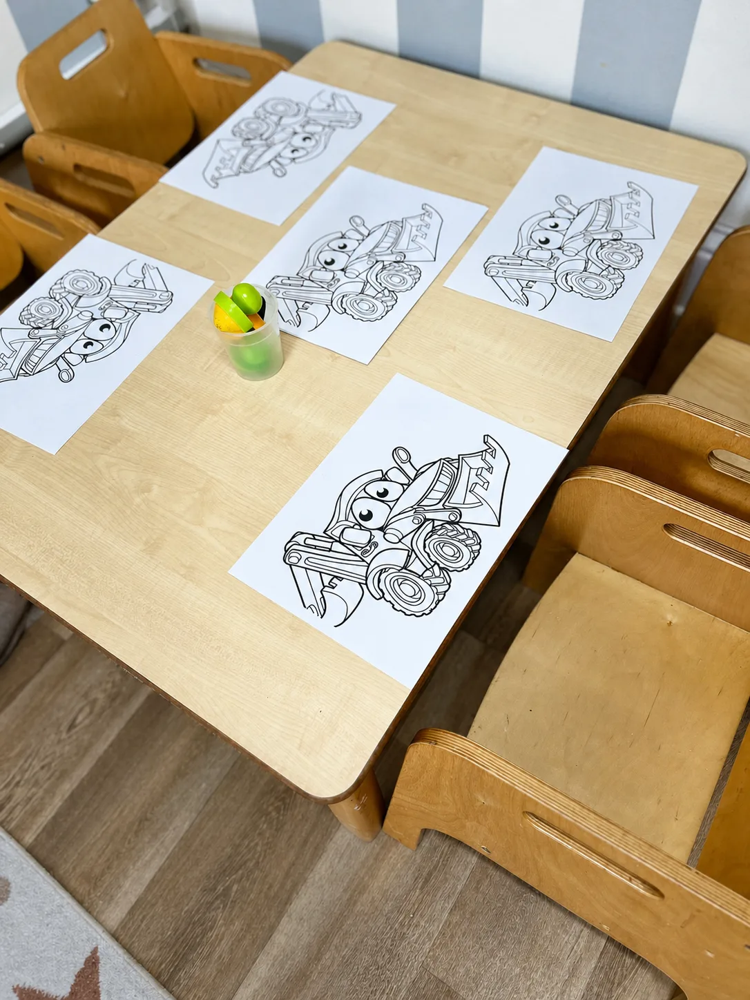 Construction vehicle colouring sheets and crayons arranged on a child-sized table
