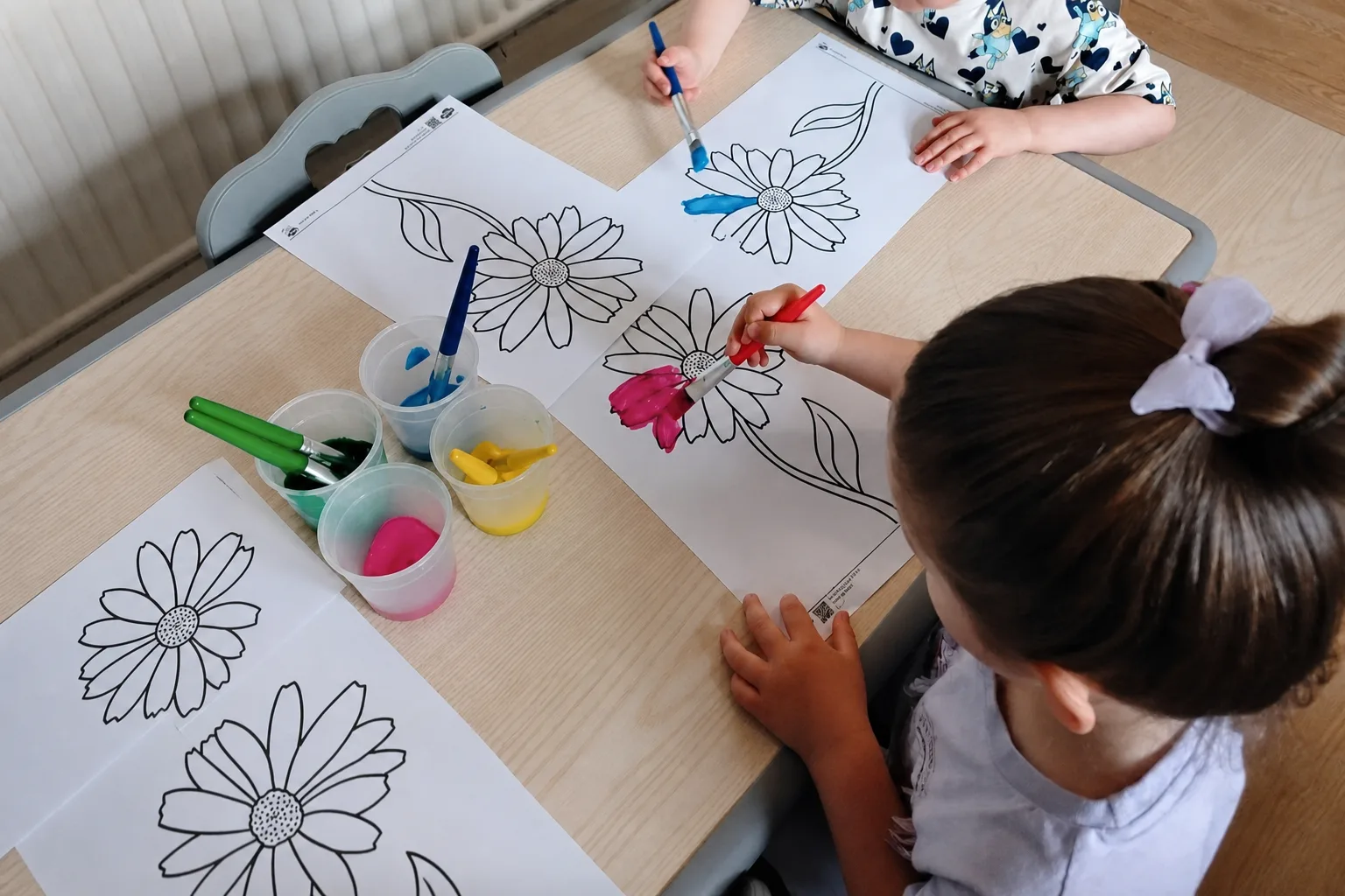 Children painting large outlined flowers together at a table