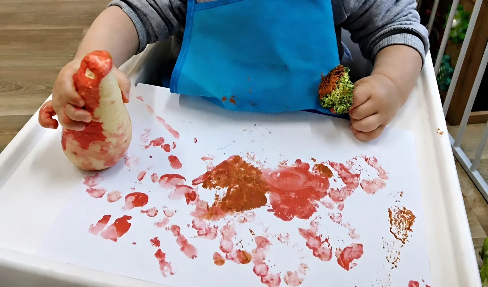 A child using a vegetable and red paint to make prints on white paper
