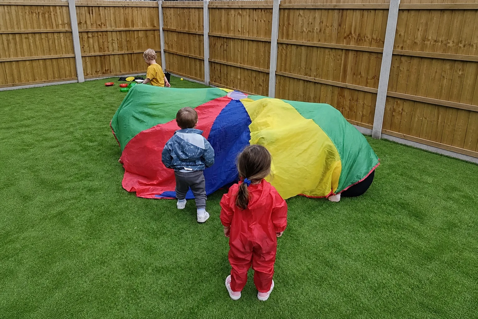 Young children playing together with a large colourful parachute in the nursery garden
